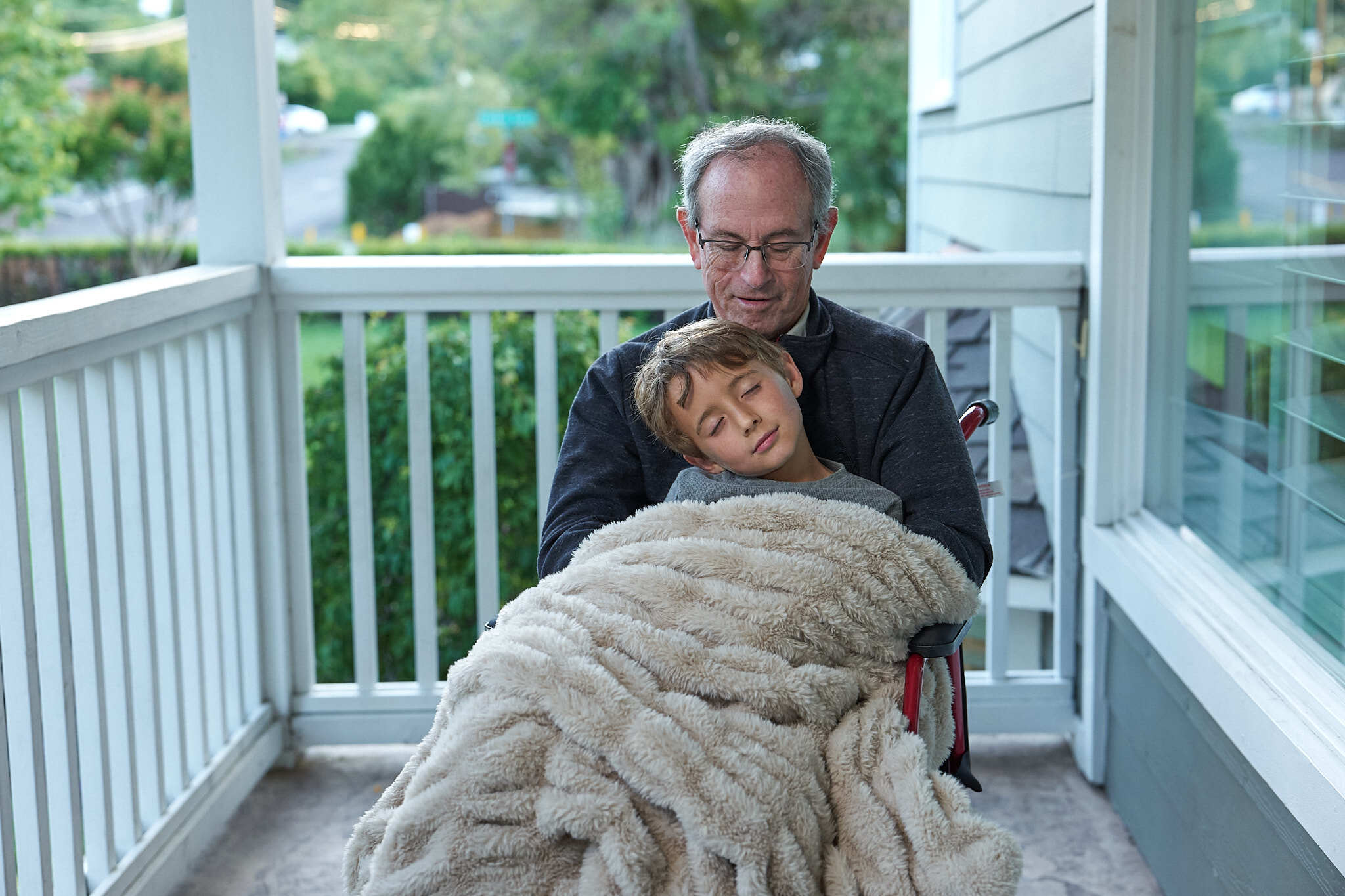 Elderly man and son cuddled together on a porch.