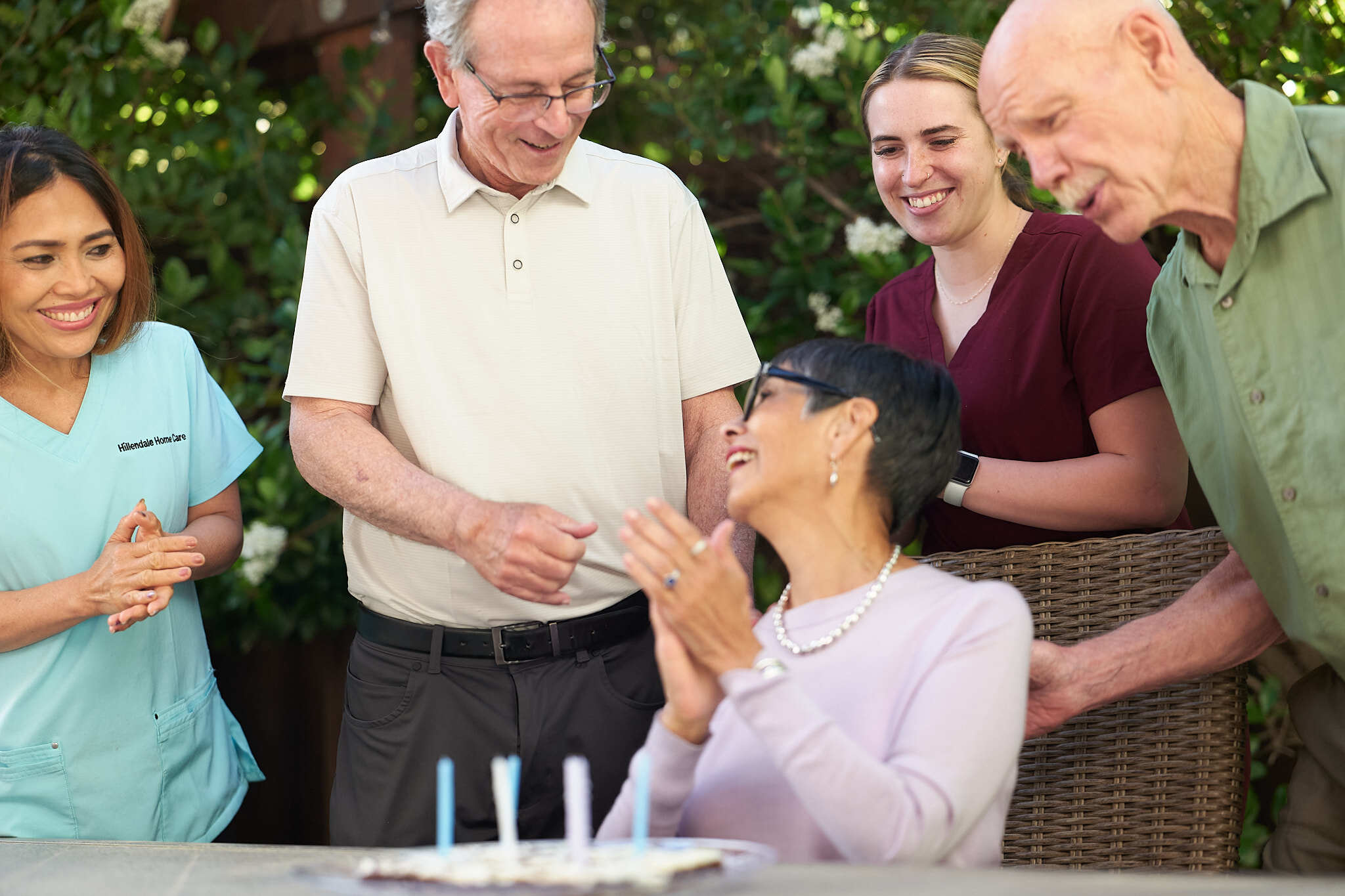 Family celebrating an elderly woman's birthday. Her caregiver is also accompanying them and celebrating.