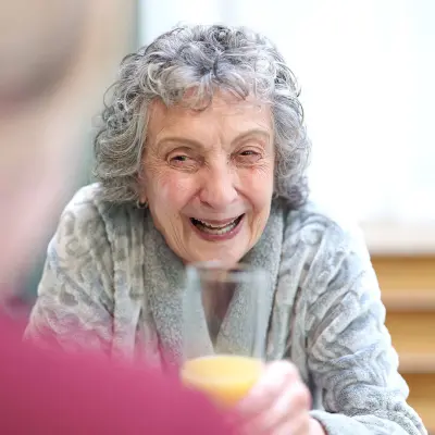 Elderly woman sipping juice and smiling.