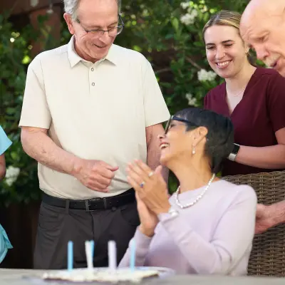 Family celebrating an elderly woman's birthday. Her caregiver is also accompanying them and celebrating.